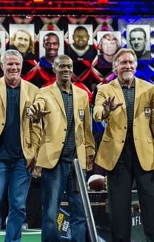 Three men in gold suits wave at a crowd on stage.