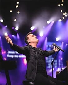 A singer at a church live concert holds his arms open.