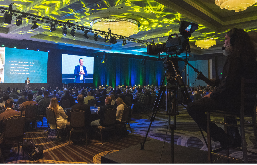corporate conference with attendees at tables and speaker on stage