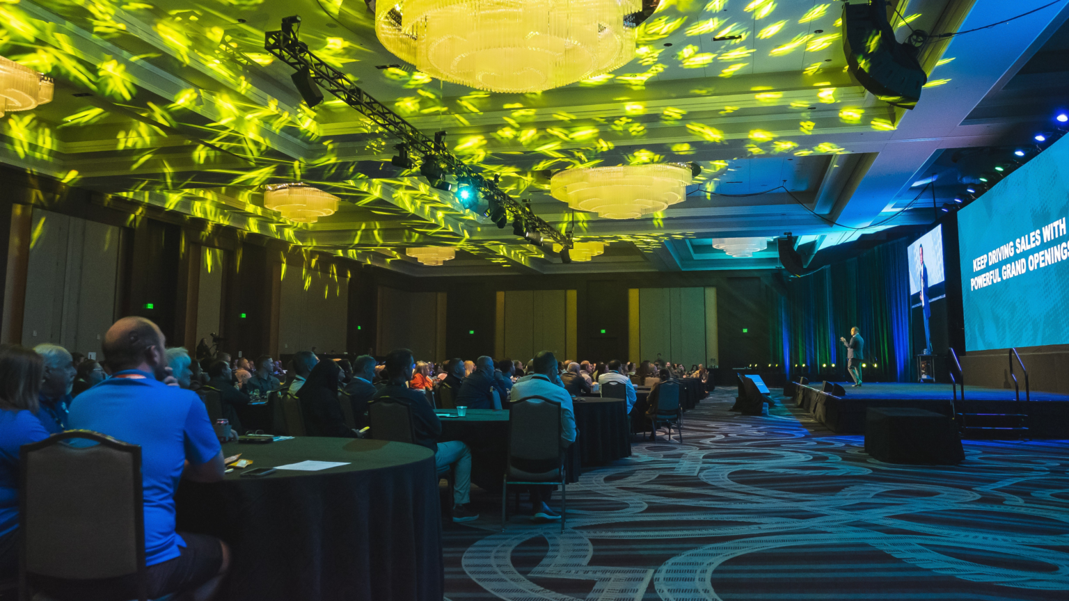 hotel ballroom with business meeting on stage and attendees in audience